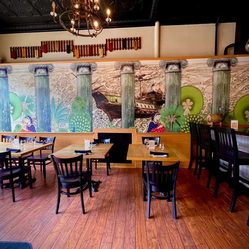 Restaurant interior with wooden tables, chairs, and a colorful mural on the wall.